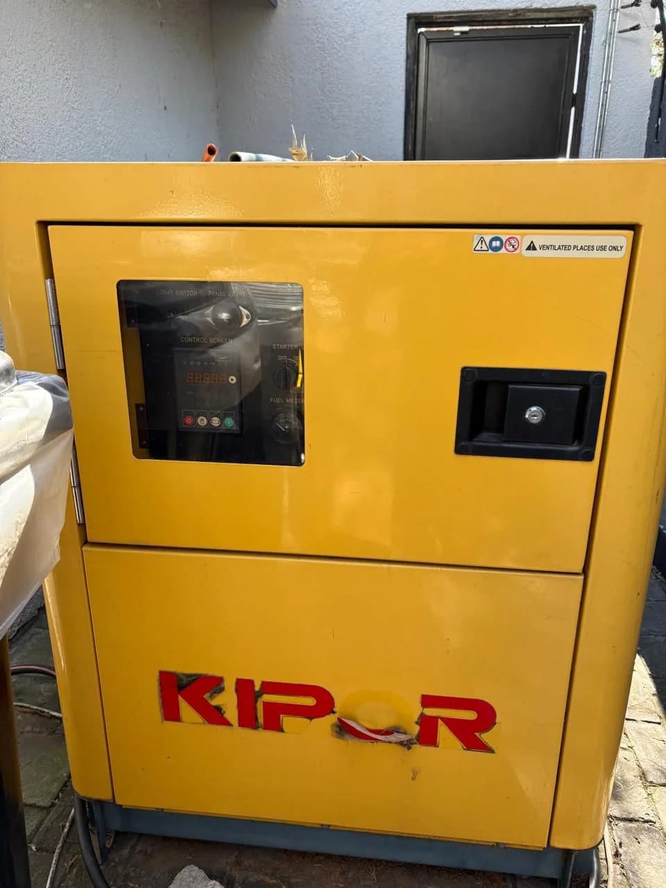 Yellow Kipor canopied diesel generator with its controller behind a window in the upper door
