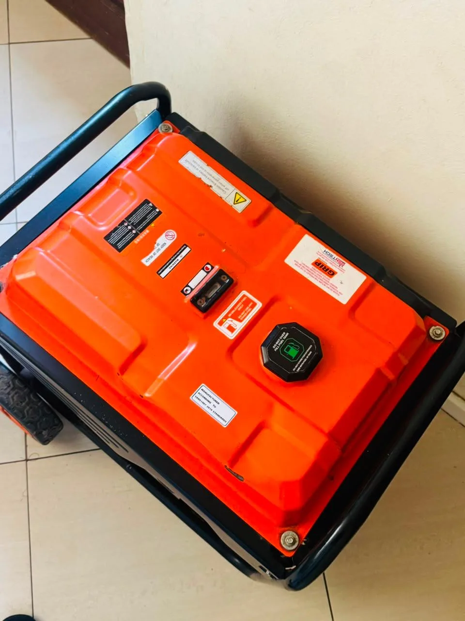 Orange fuel tank of a Grip portable petrol generator seen from above, with fuel cap, gauge and warning labels