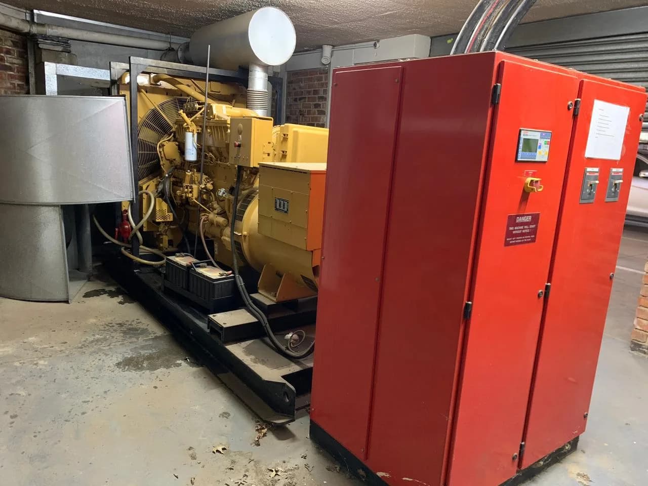 Yellow open diesel generator set beside a red control cabinet with digital controller and breakers in a basement plant room