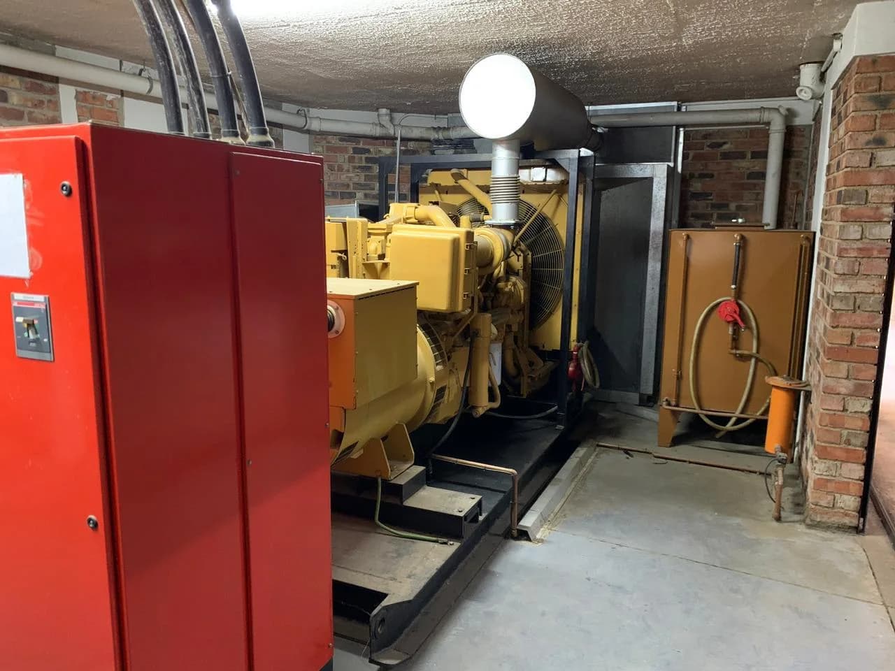 Yellow open diesel generator set with exhaust silencer and day tank in a face-brick basement plant room