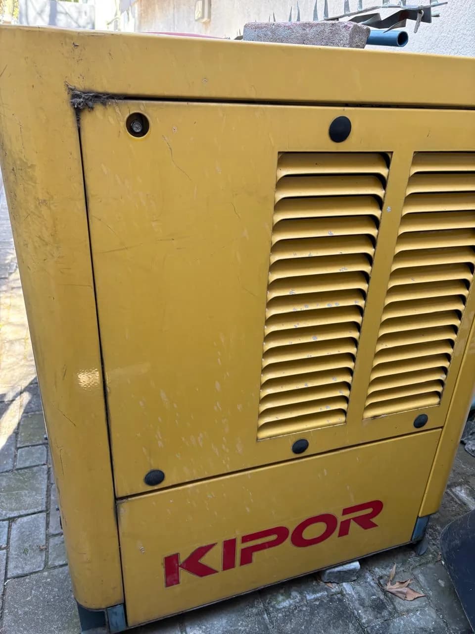Worn yellow Kipor diesel generator canopy with louvred door panels and a brick resting on the roof