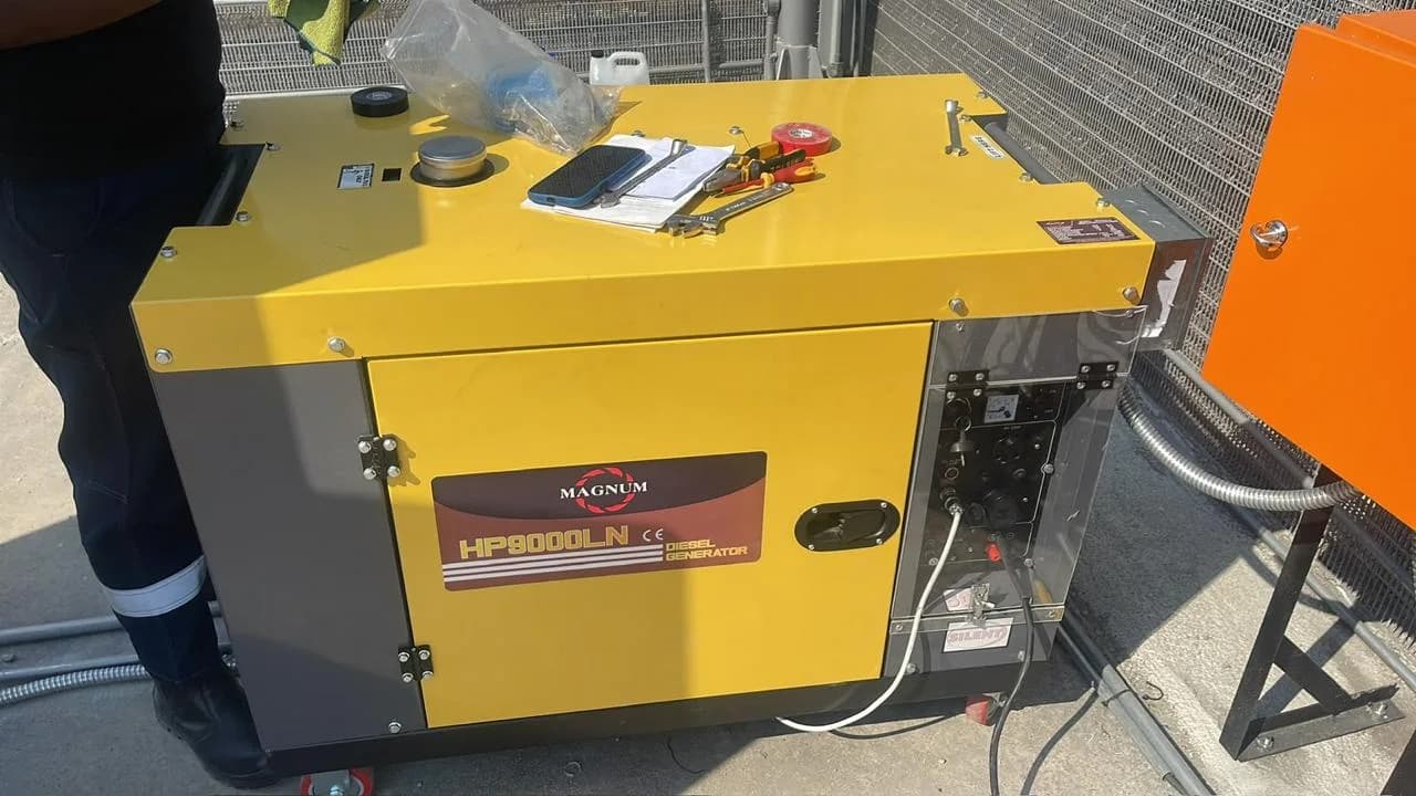 Yellow Magnum HP9000LN silent diesel generator with tools and paperwork on top, one person standing beside it
