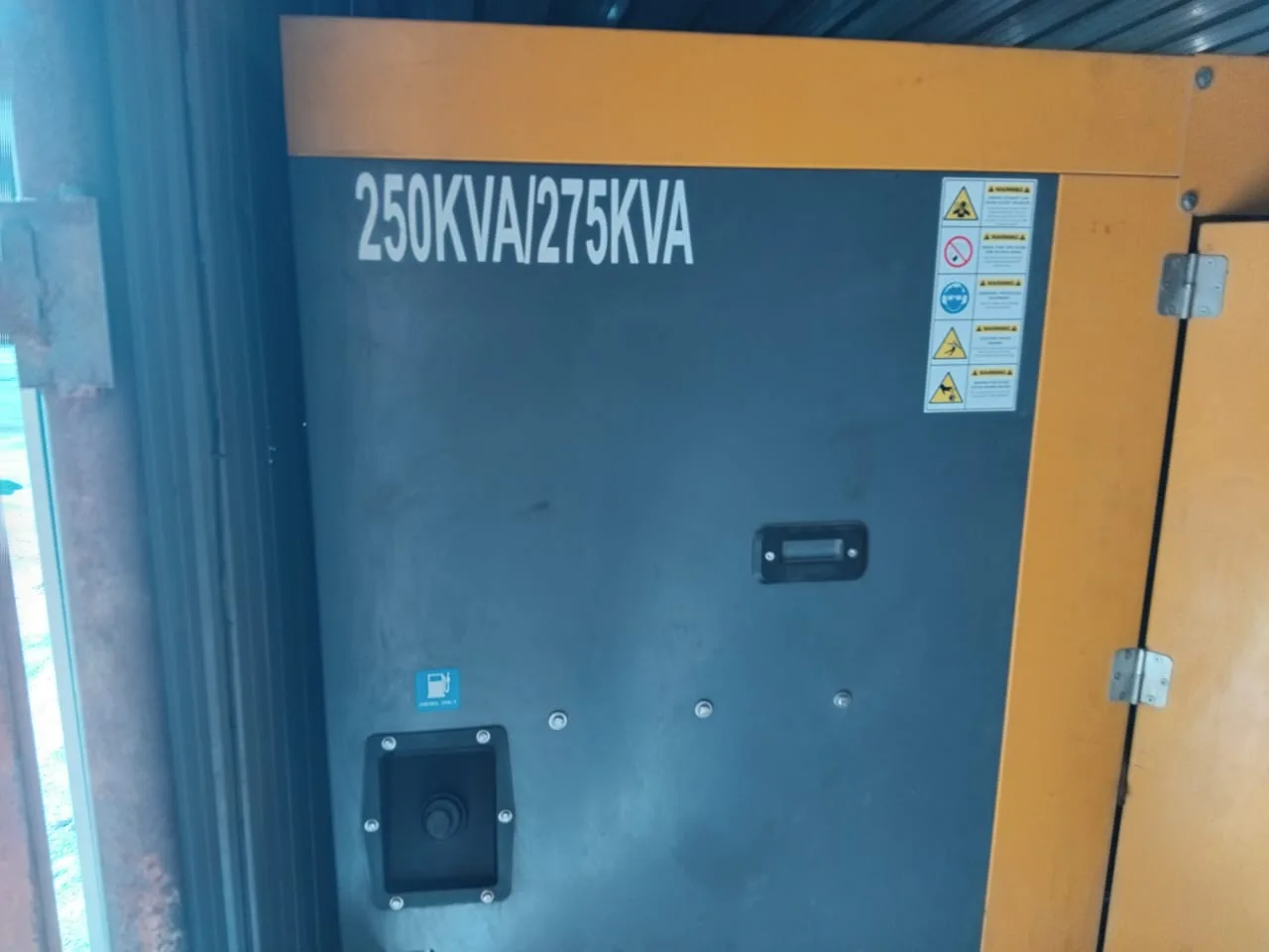 Grey and orange canopy end panel marked 250KVA/275KVA with safety pictogram labels and a fuel filler point