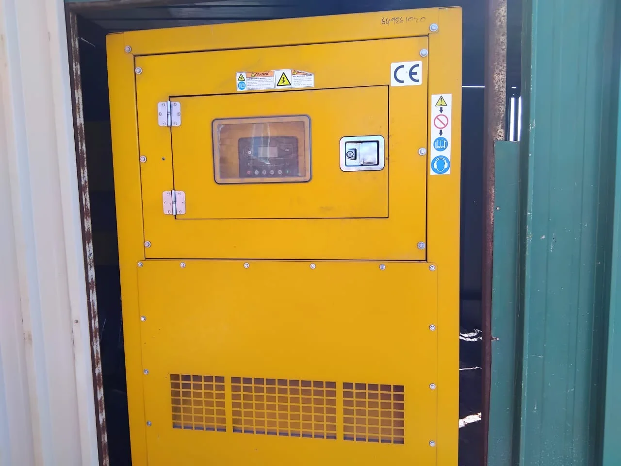 Yellow canopied diesel generator front with a controller behind a window, CE mark and safety labels