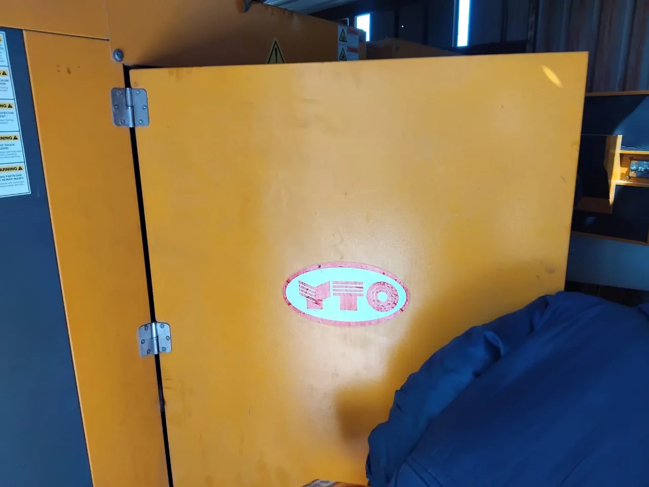 Orange canopy door bearing a YTO logo, with a blue cover draped in front, inside a dim container