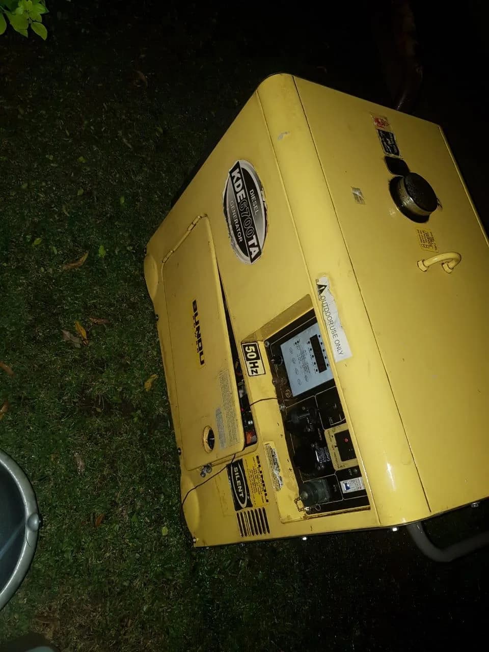 Yellow Bundu Power KDE6700TA silent diesel generator lying on grass at night, lit by camera flash