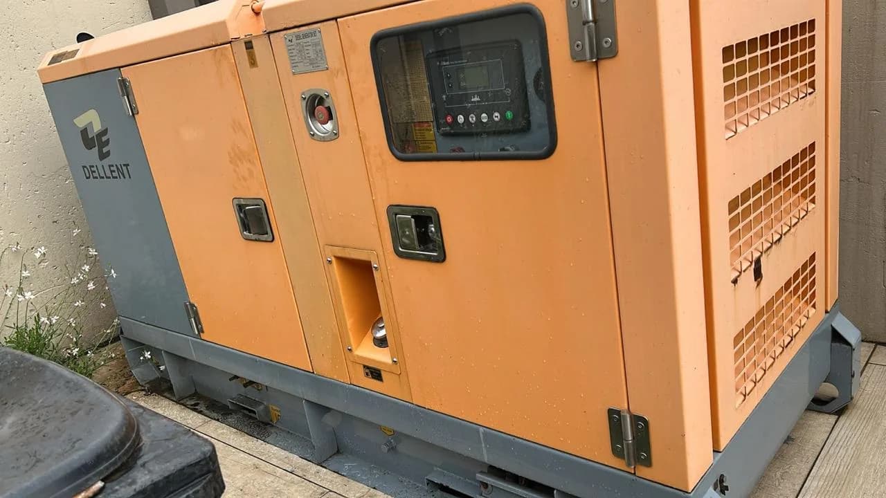 Orange Dellent canopied diesel generator with a digital controller behind a window, on tiles beside a wall