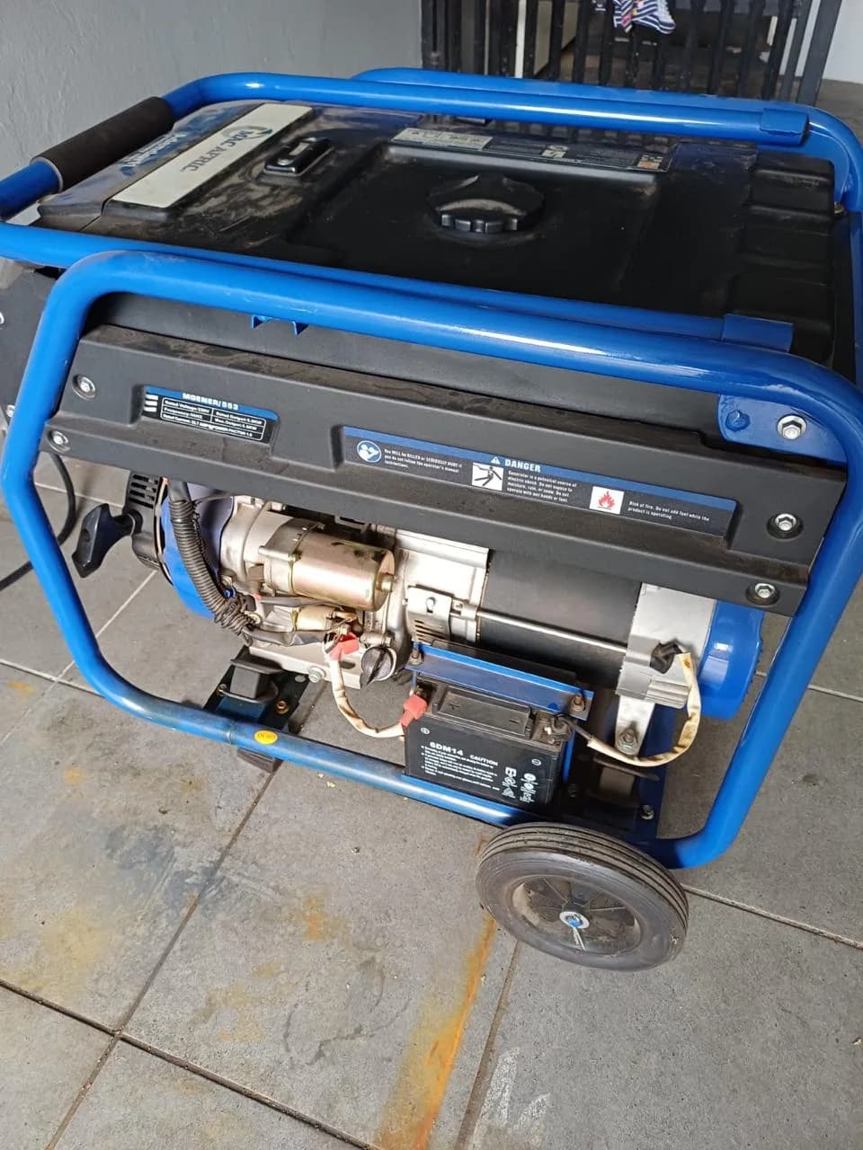 Mac Afric portable generator in a blue tube frame with electric starter and battery, on a tiled patio