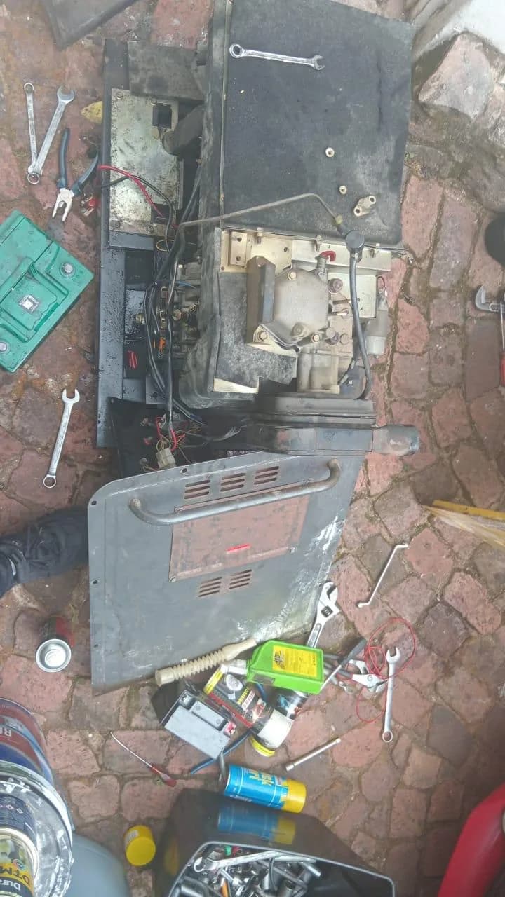 Small diesel generator stripped down on brick paving with spanners, pliers and parts spread around it