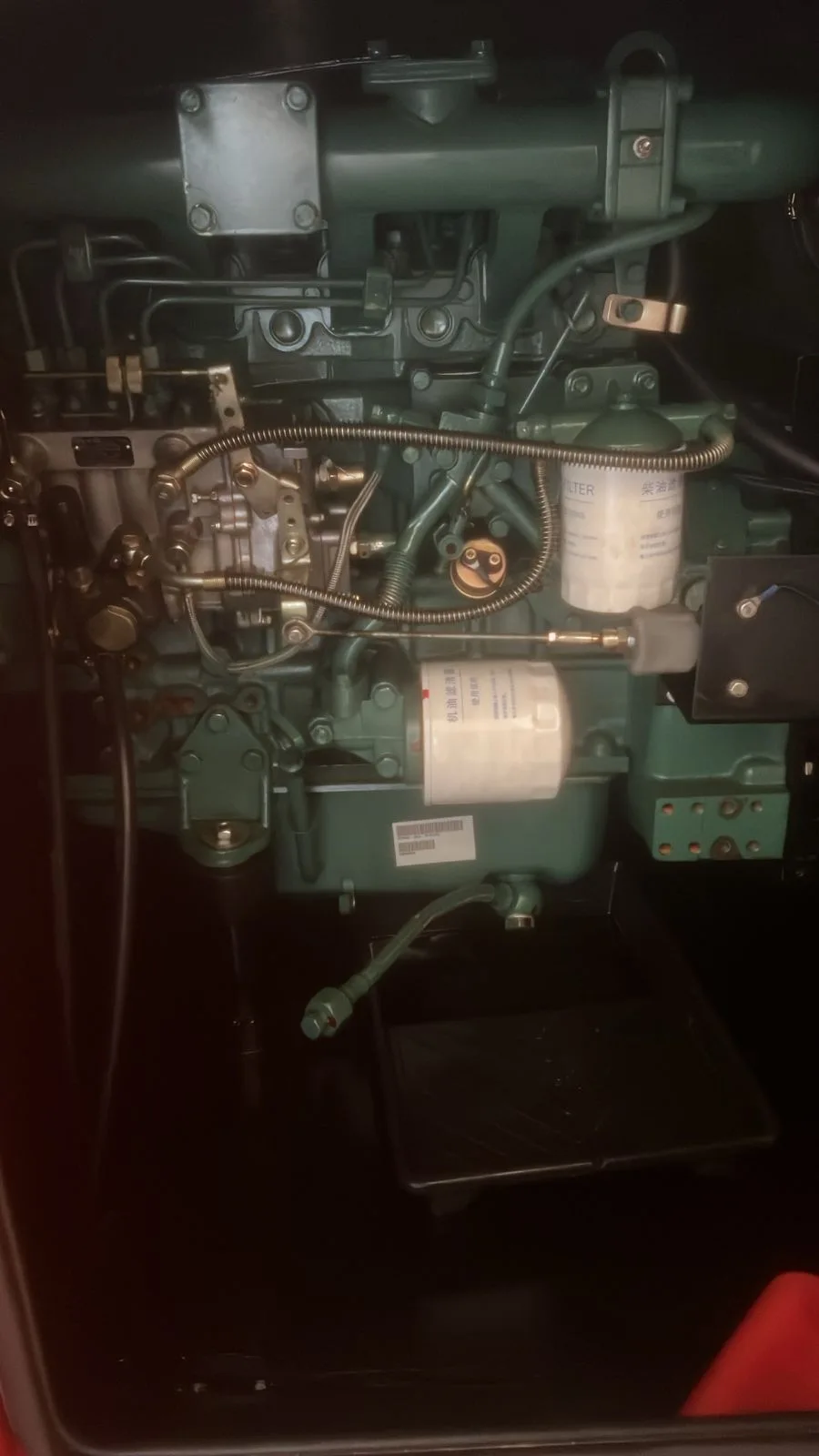 Green four-cylinder diesel engine with injection lines, fuel filter and oil filter inside a dark canopy