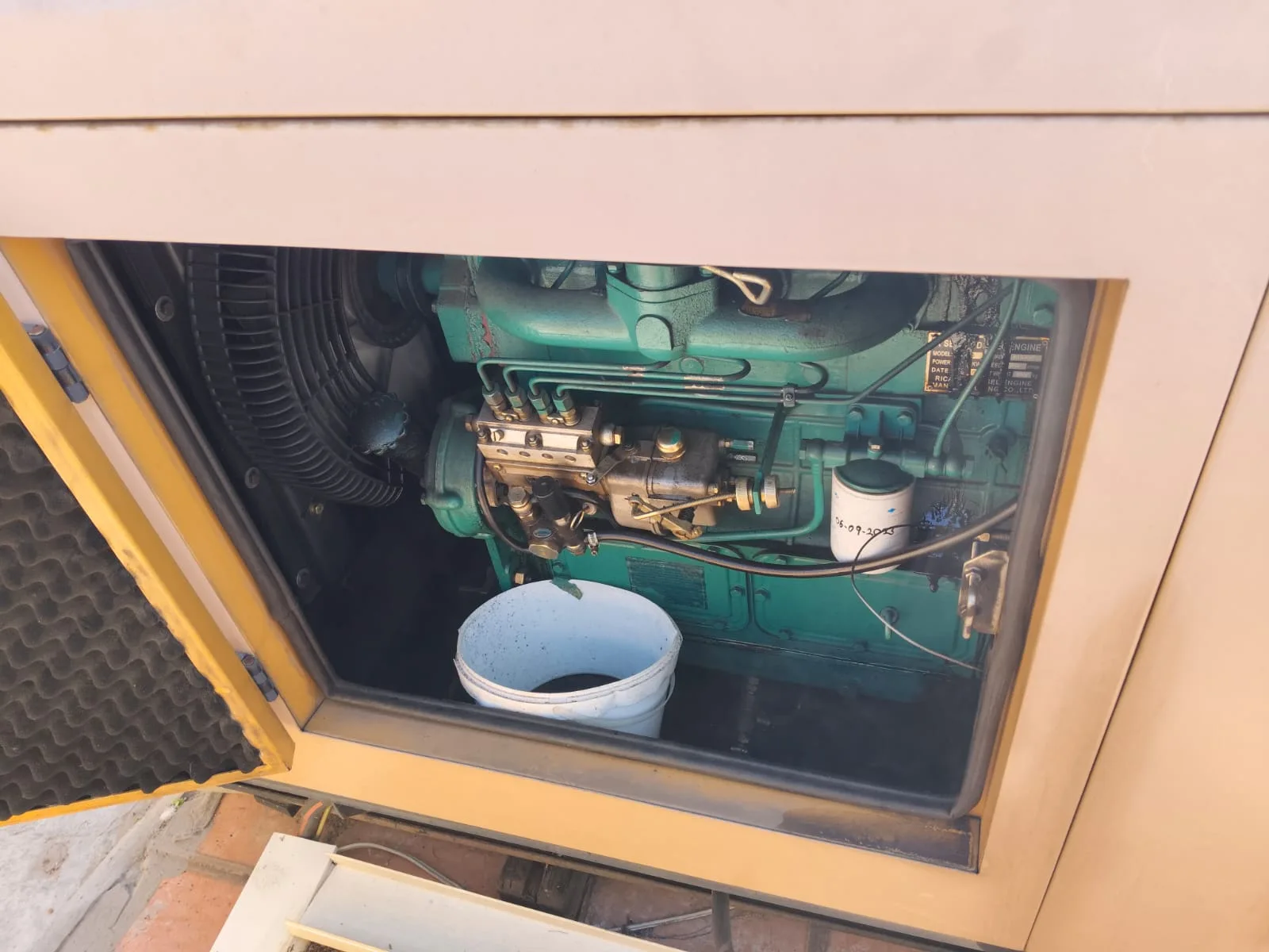 Canopy door open on a green four-cylinder diesel engine with injection pump, a bucket below to catch drained oil