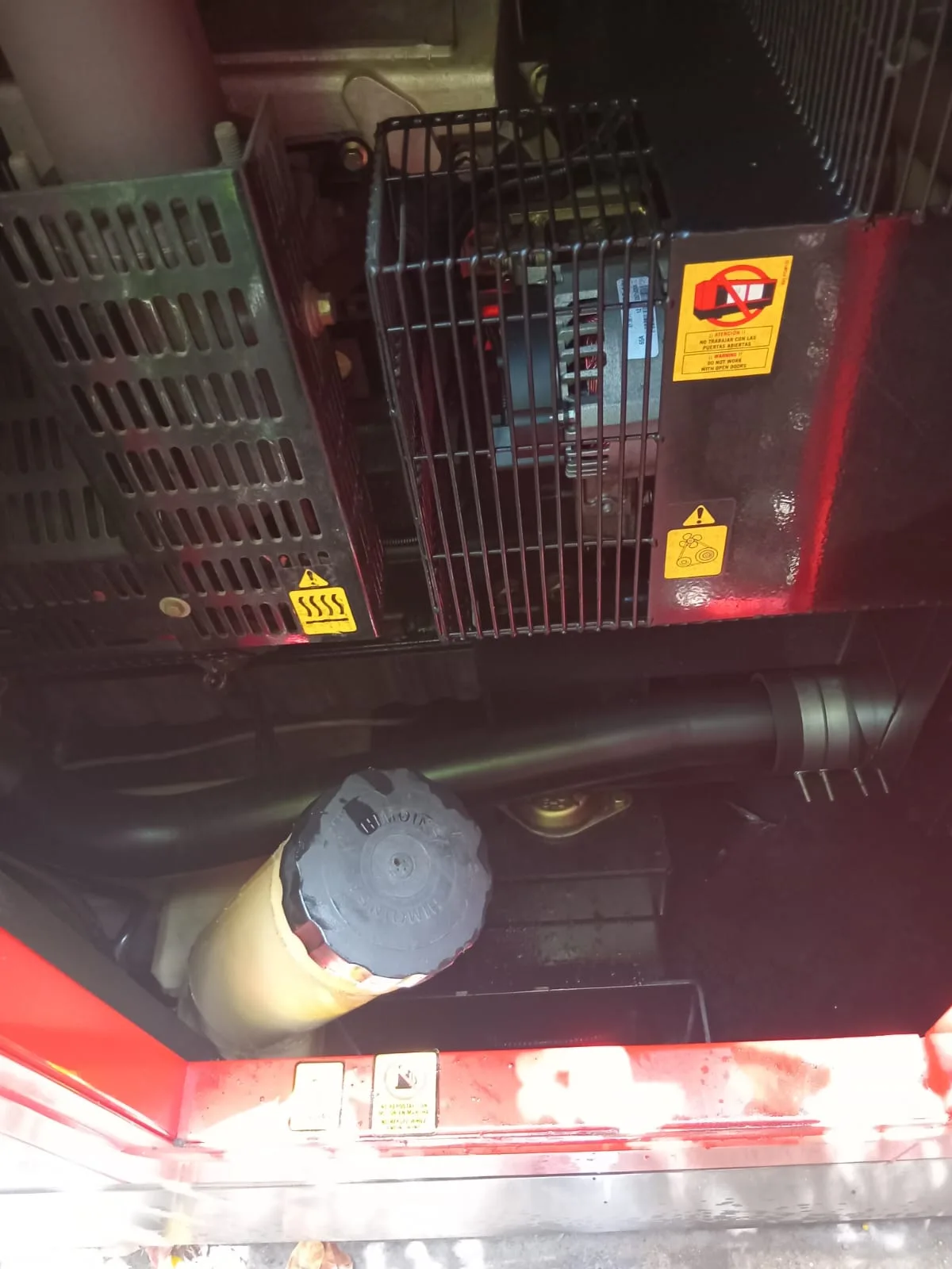 Inside a red canopy: radiator fan guard, warning labels and air filter above the engine sump