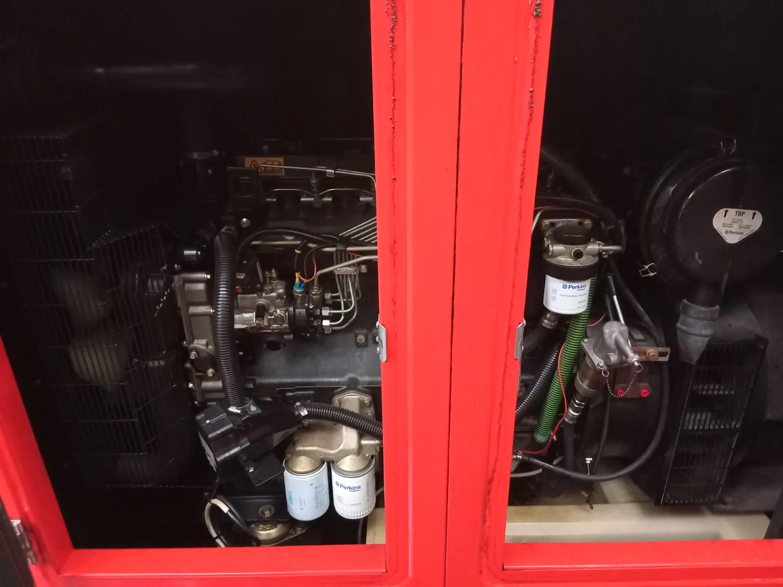 Red canopy doors open on a black diesel engine with Perkins fuel and oil filters and an air cleaner