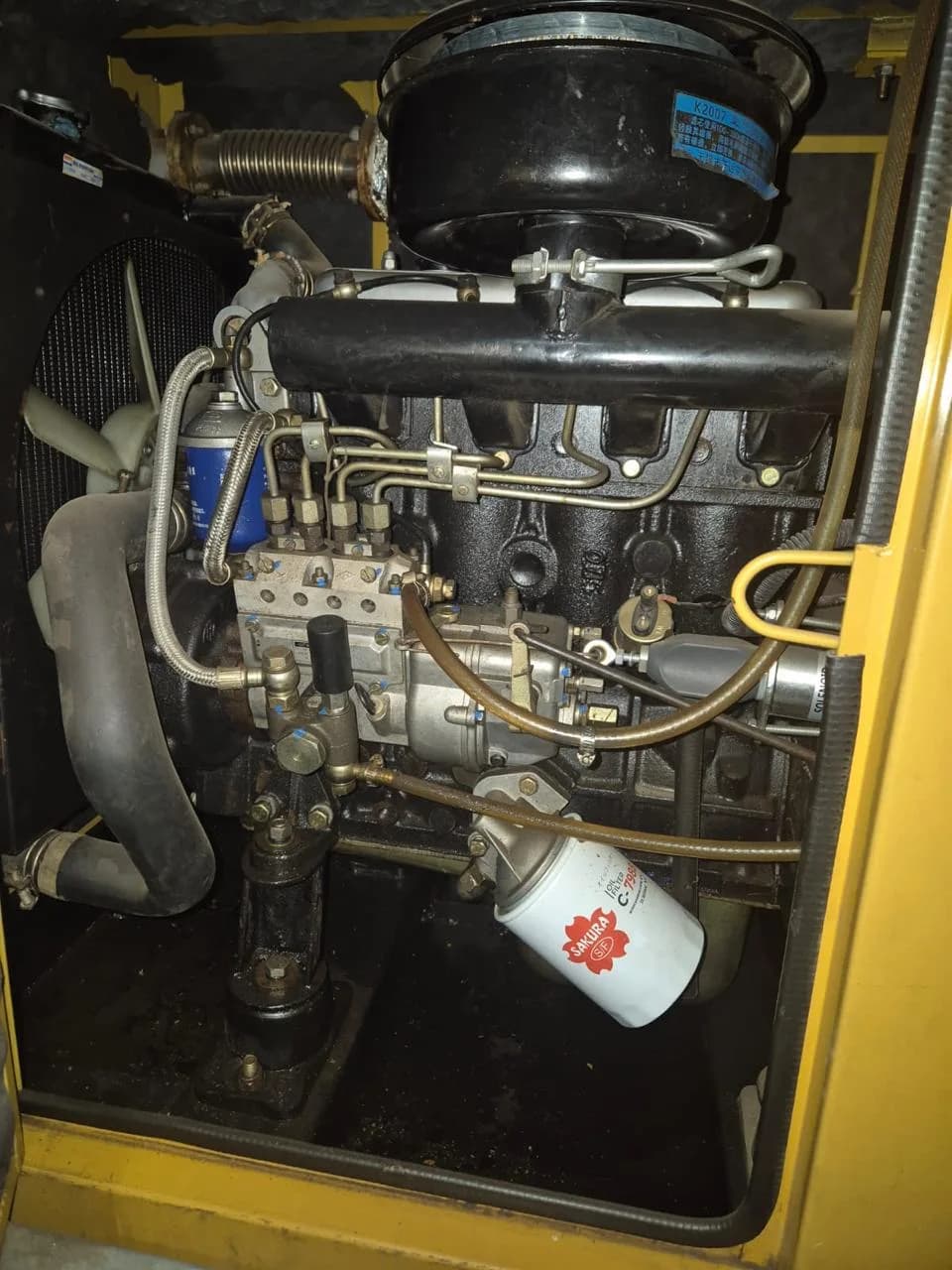 Black diesel engine with injection pump, Sakura oil filter and round air cleaner inside a yellow canopy