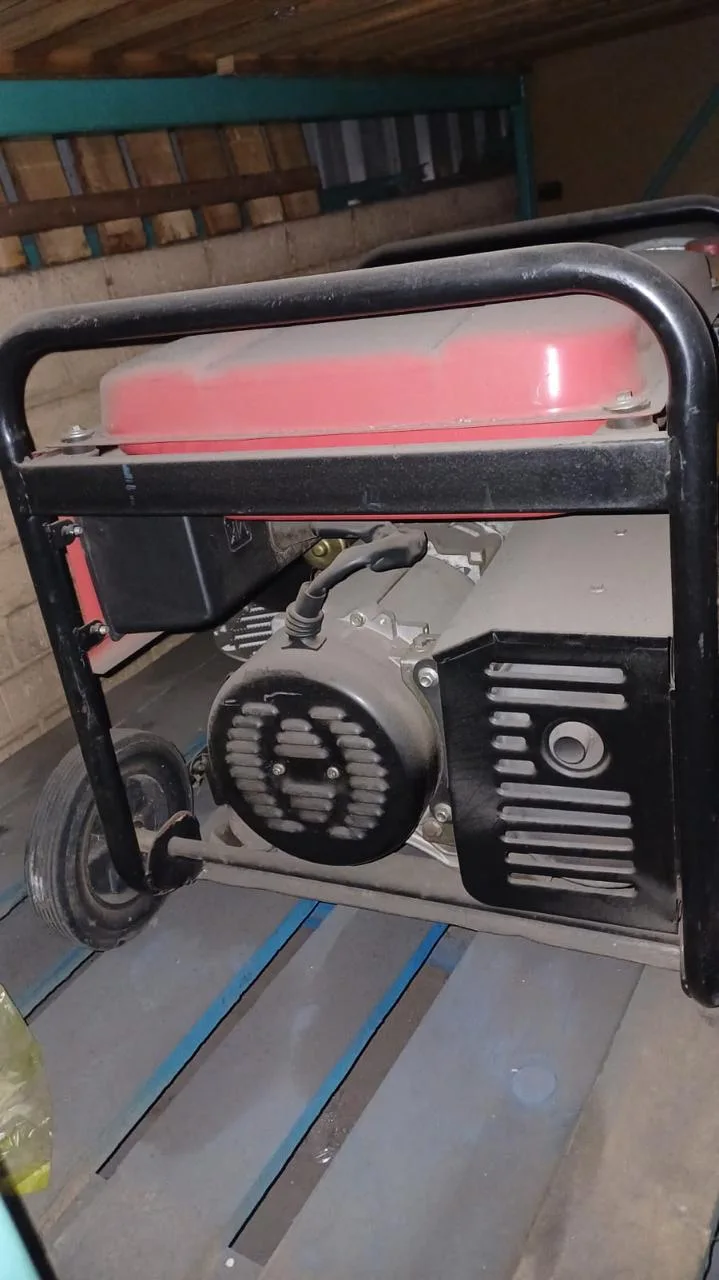 Red-tanked portable generator in a black wheeled frame standing on a timber floor