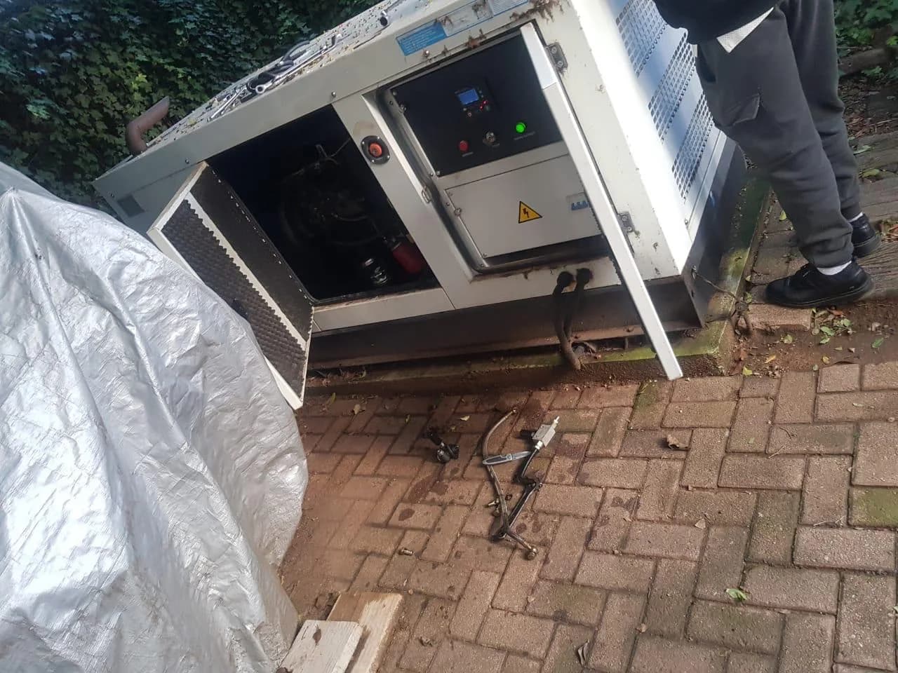 White canopied diesel generator with doors open on its controller, one person standing beside it on brick paving