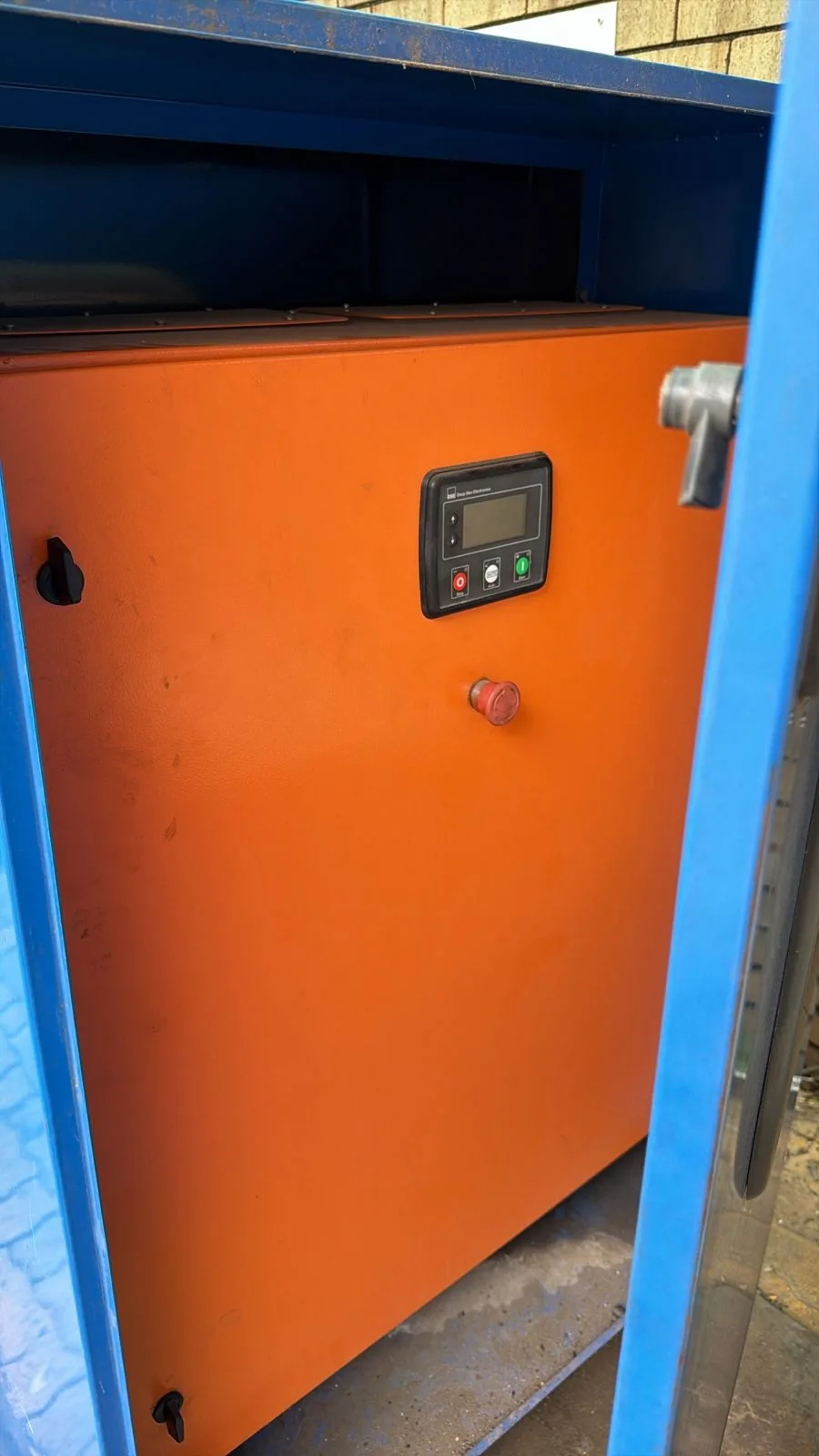 Orange control box with a Deep Sea Electronics controller and emergency stop inside an open blue canopy door