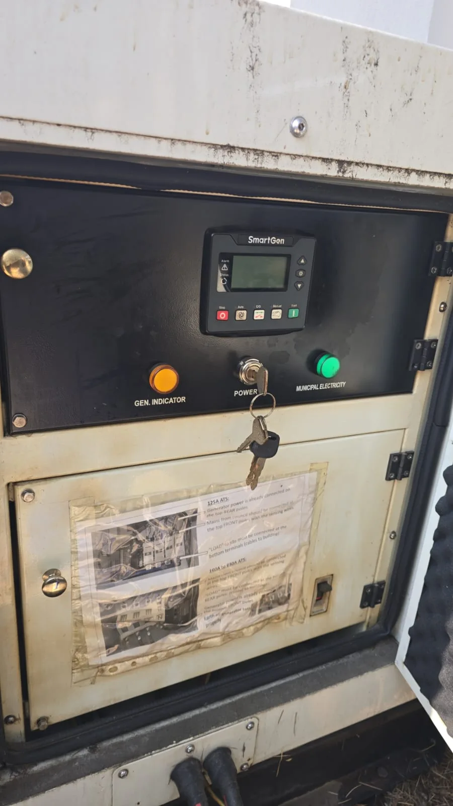 SmartGen controller with key switch and indicator lights above a taped-on ATS wiring instruction sheet