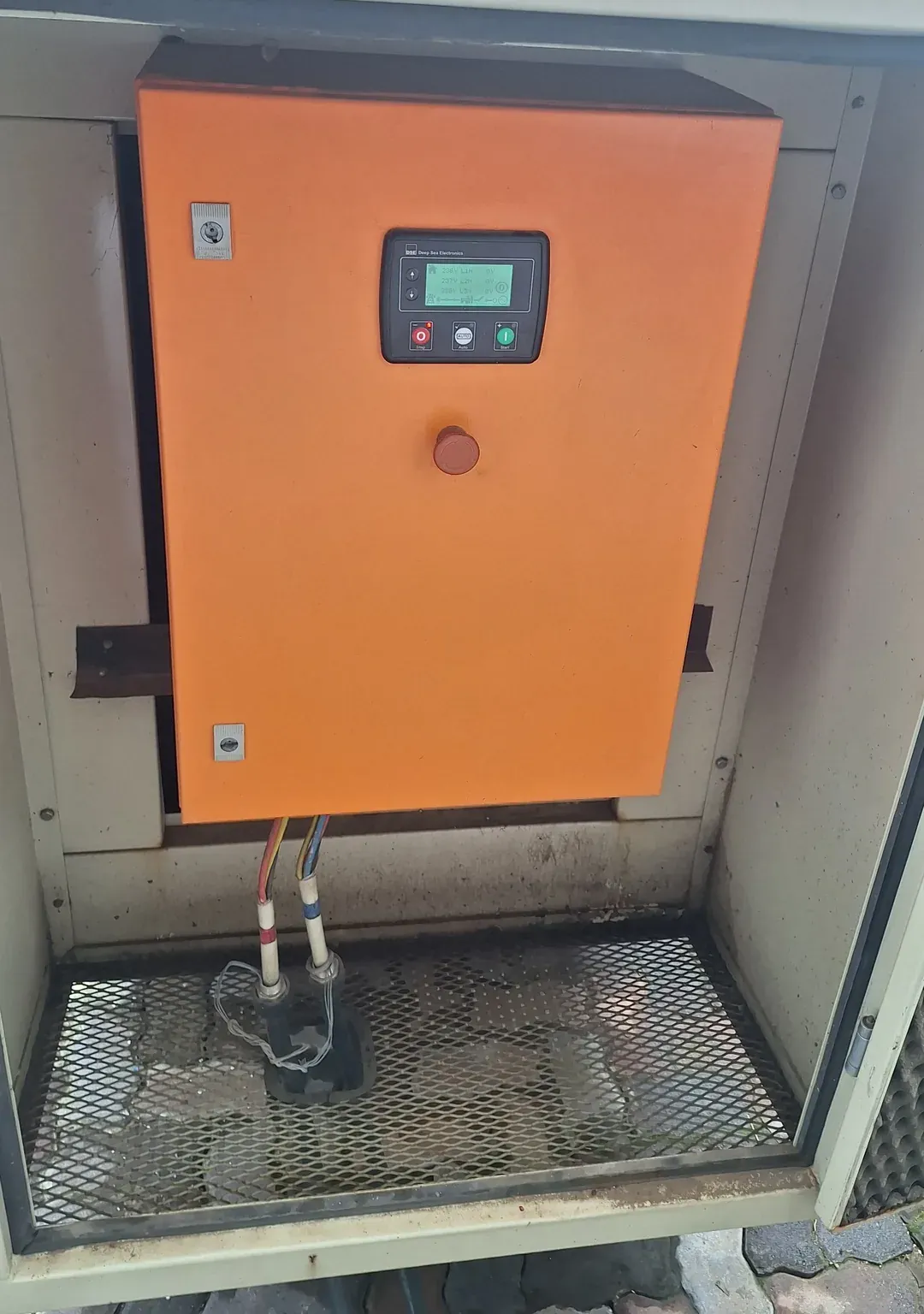 Orange control panel with a Deep Sea Electronics controller and emergency stop inside an open grey enclosure