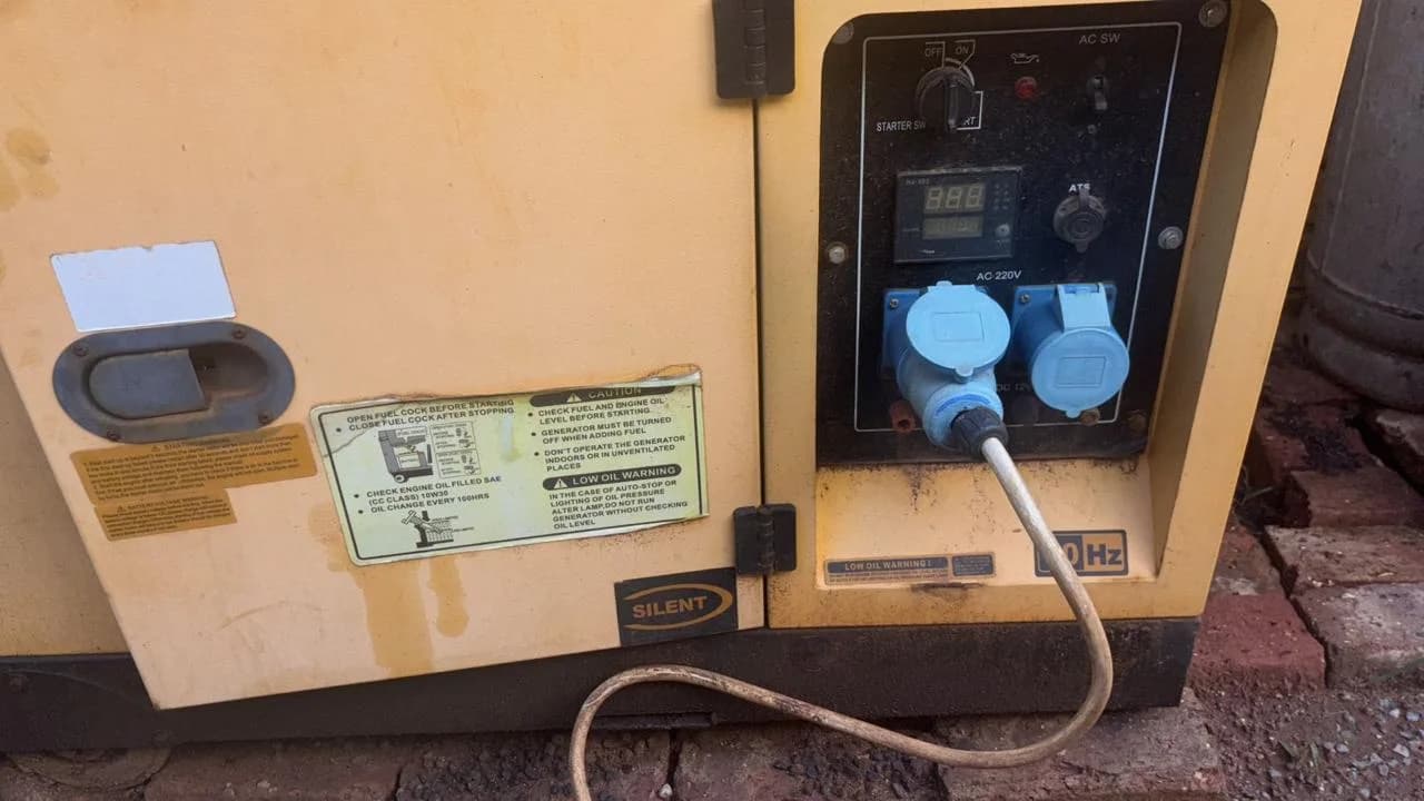 Side of a cream silent diesel generator with digital meter, two blue industrial sockets and a plugged-in lead
