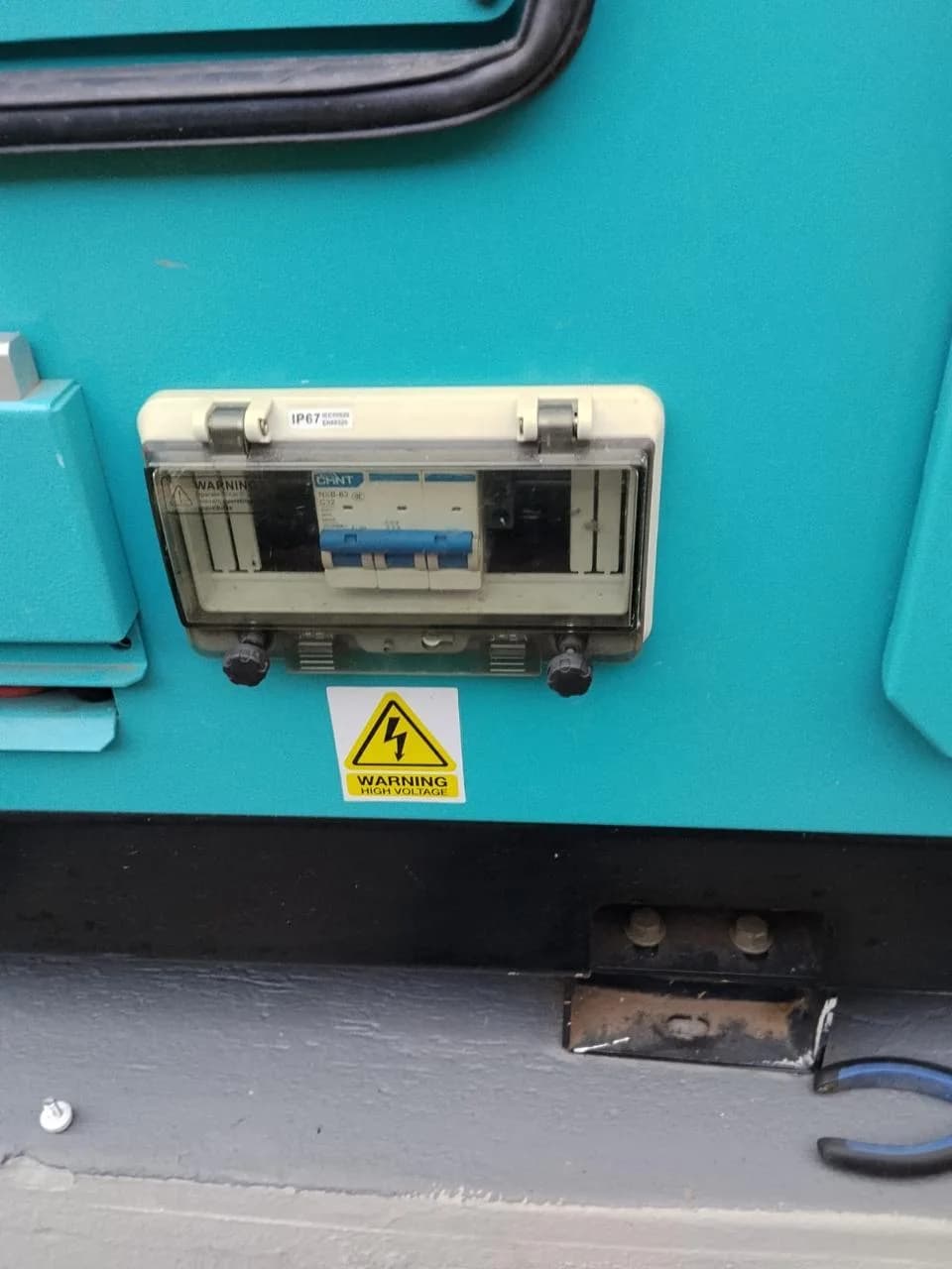 Weatherproof breaker box with a CHINT circuit breaker and high-voltage warning on a teal generator canopy