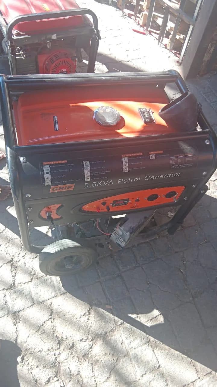 Black and orange Grip 5.5 kVA petrol generator with its side panel off, standing on sunlit paving