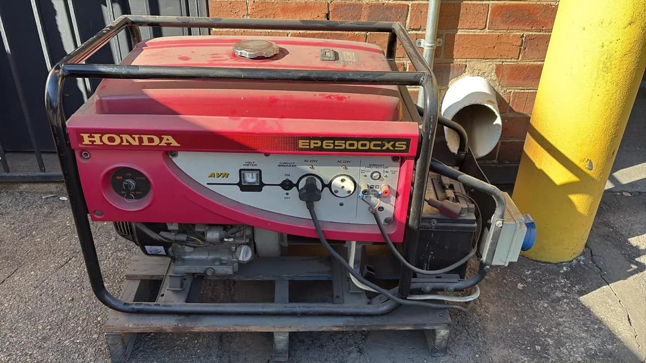 Red Honda EP6500CXS petrol generator on a pallet, plugged in and wired to a changeover box against a brick wall