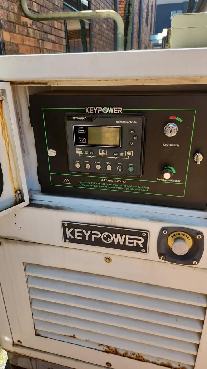 Keypower genset controller with key switch and voltage adjuster above an emergency stop on a white canopy