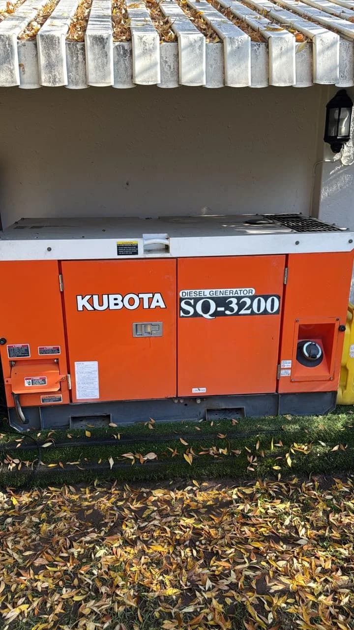 Orange Kubota SQ-3200 silent diesel generator on artificial grass under a concrete pergola, autumn leaves in front