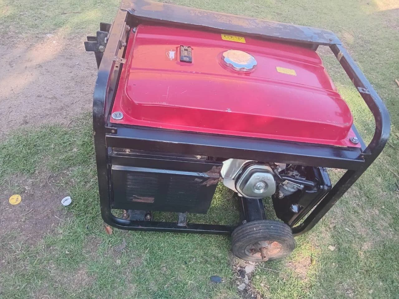 Red-tanked portable generator in a rust-marked black frame standing on patchy grass