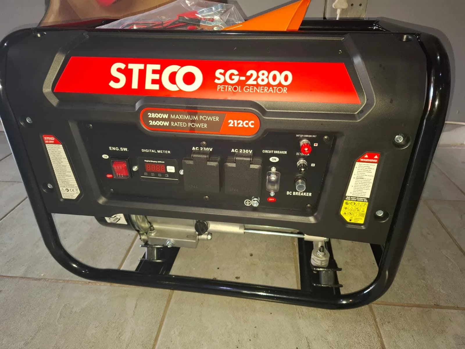 Black and red Steco SG-2800 petrol generator showing its digital meter, two 230 V sockets and breakers on a tiled floor